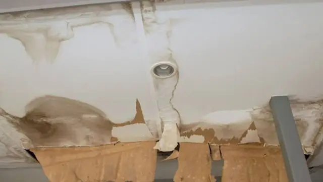 Stained and sagging ceiling around a light fixture with exposed damaged material