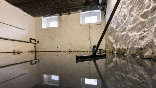 Damp basement with standing water on the floor, a squeegee in the foreground and stained masonry walls